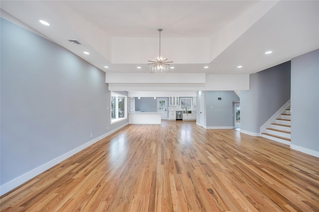 unfurnished living room with light wood finished floors, baseboards, visible vents, stairs, and a notable chandelier