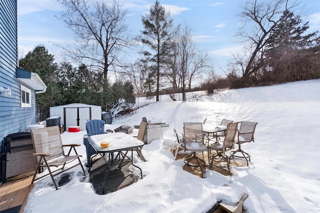 snow covered patio with an outbuilding, a storage unit, and outdoor dining space