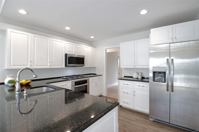 kitchen featuring light wood finished floors, stainless steel appliances, tasteful backsplash, white cabinets, and a sink