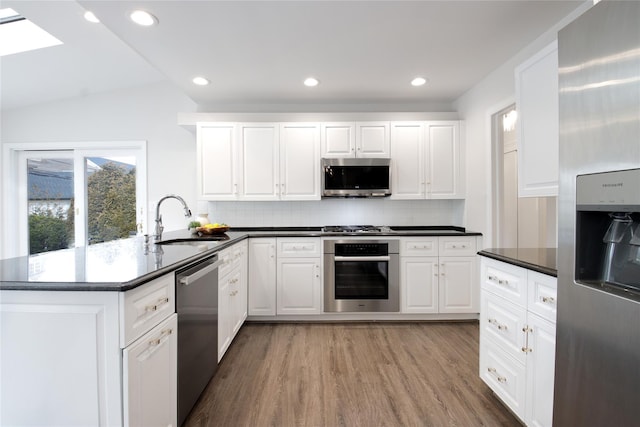 kitchen featuring tasteful backsplash, dark countertops, appliances with stainless steel finishes, wood finished floors, and a sink