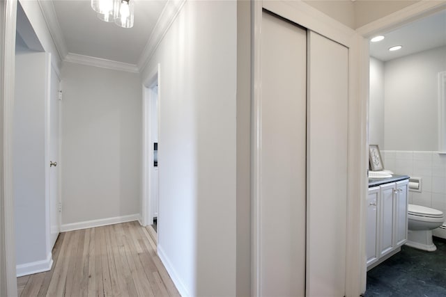 corridor featuring light wood finished floors, baseboards, ornamental molding, tile walls, and recessed lighting