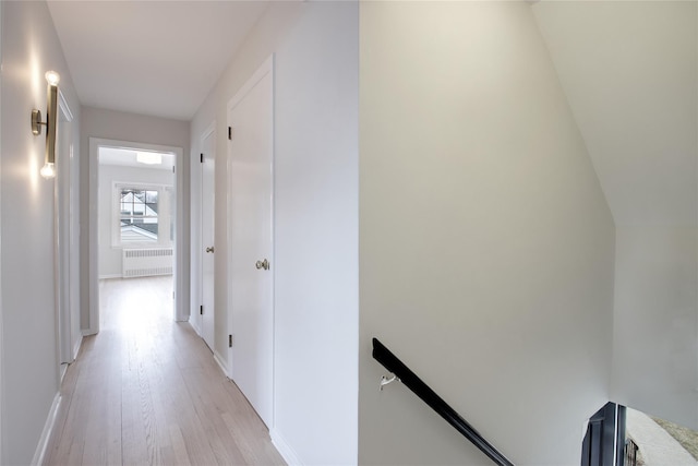 corridor with radiator, light wood-style floors, and an upstairs landing