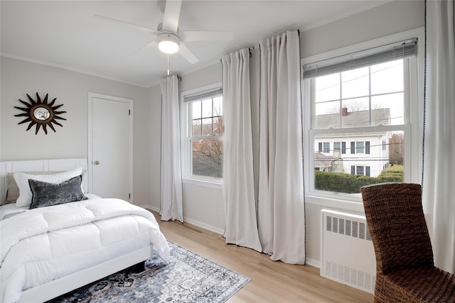 bedroom with light wood-style floors, baseboards, radiator heating unit, and a ceiling fan