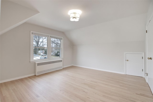 additional living space with lofted ceiling, baseboards, light wood-style flooring, and radiator