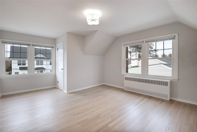 additional living space with vaulted ceiling, light wood-type flooring, baseboards, and radiator