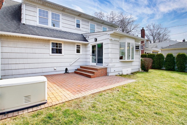 back of property with a shingled roof, a wall unit AC, a chimney, a yard, and a patio area