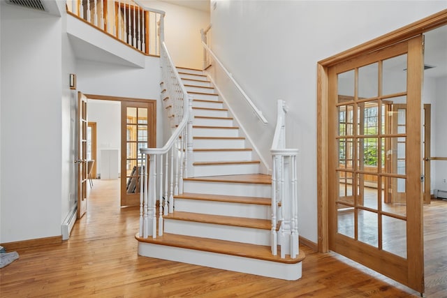 97 Ludlam Rd, Monroe, NY 10950 - staircase featuring french doors, wood finished floors, a high ceiling, baseboards, and a baseboard heating unit