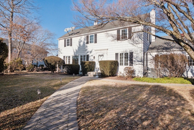 colonial-style house featuring a chimney and a front yard