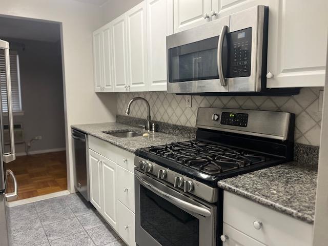 kitchen featuring stone counters, a sink, white cabinets, appliances with stainless steel finishes, and backsplash