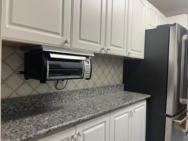 kitchen with tasteful backsplash, freestanding refrigerator, white cabinets, and dark stone countertops