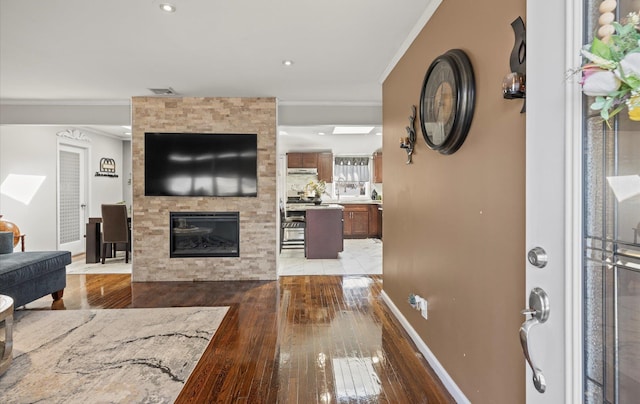 living room with a large fireplace, visible vents, baseboards, wood-type flooring, and crown molding