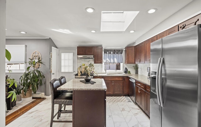 kitchen featuring a baseboard radiator, under cabinet range hood, a sink, marble finish floor, and appliances with stainless steel finishes