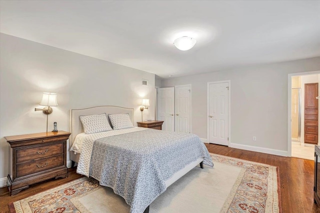 bedroom featuring visible vents, baseboards, dark wood finished floors, and ensuite bathroom