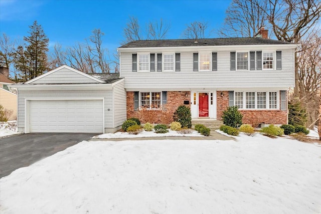 colonial house featuring aphalt driveway, brick siding, a chimney, and an attached garage