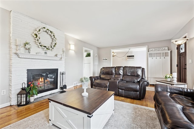 living room featuring a brick fireplace, light wood-style flooring, baseboards, and a wall mounted air conditioner