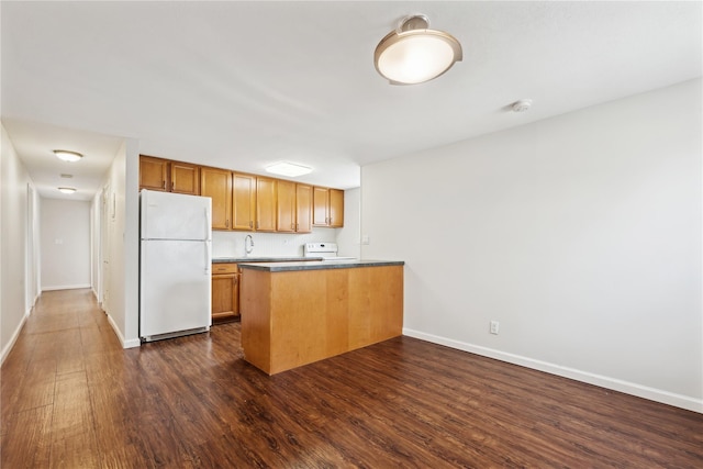 kitchen featuring a peninsula, white appliances, dark wood-type flooring, baseboards, and brown cabinetry