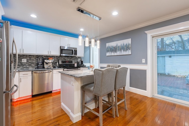 kitchen featuring stainless steel appliances, white cabinetry, ornamental molding, a center island, and decorative light fixtures