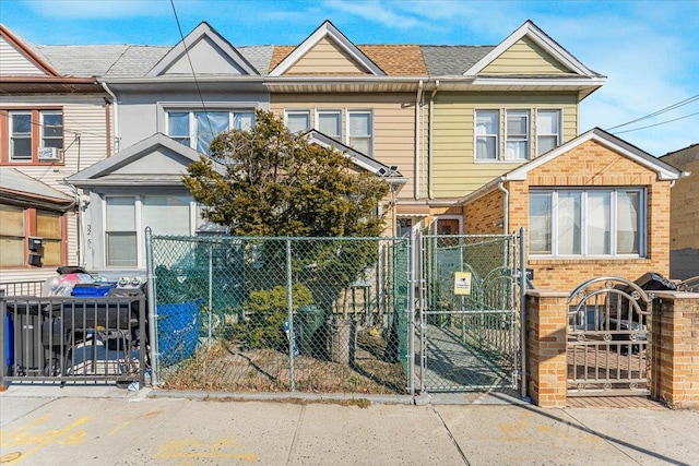 townhome / multi-family property with a fenced front yard, a gate, brick siding, and roof with shingles