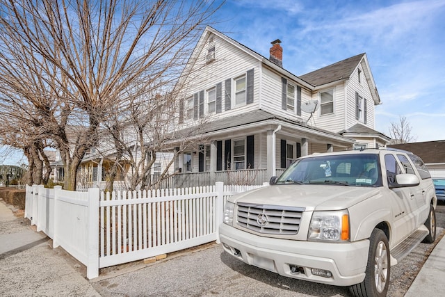 view of front of house with a porch, a fenced front yard, and a chimney