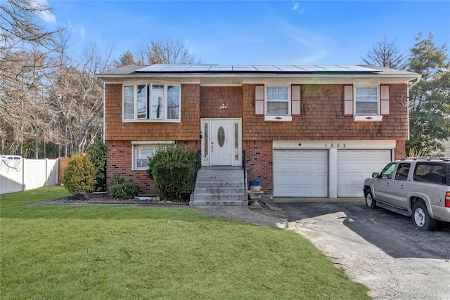 bi-level home with roof mounted solar panels, fence, aphalt driveway, and a front yard