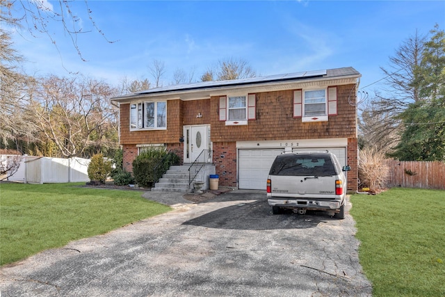 bi-level home featuring a front yard, roof mounted solar panels, fence, a garage, and driveway