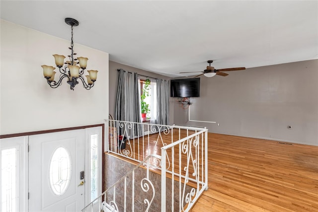 foyer with wood finished floors and ceiling fan with notable chandelier