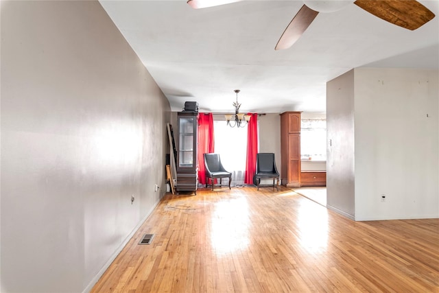 unfurnished room featuring light wood-style floors, visible vents, baseboards, and ceiling fan with notable chandelier