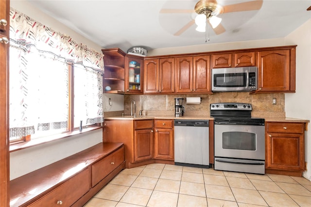 kitchen featuring stainless steel appliances, light countertops, backsplash, brown cabinetry, and glass insert cabinets