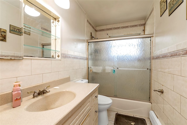 full bathroom featuring a baseboard radiator, toilet, bath / shower combo with glass door, vanity, and tile walls