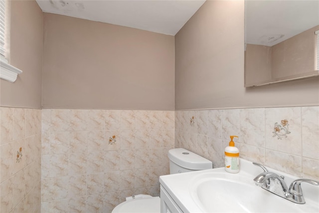 half bath with toilet, wainscoting, vanity, and tile walls