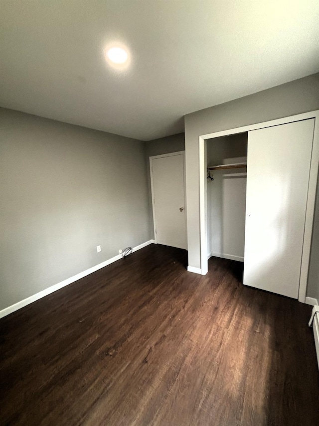 unfurnished bedroom with dark wood-style flooring, a closet, and baseboards