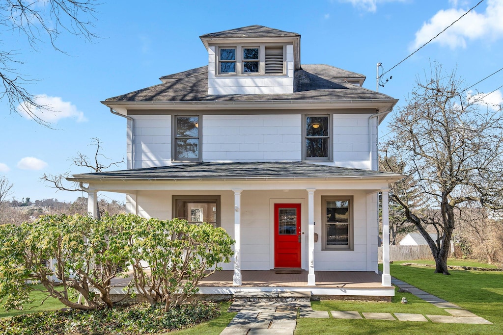 american foursquare style home with roof with shingles, a porch, a front lawn, and fence