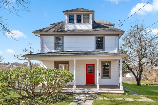 american foursquare style home with roof with shingles, a porch, a front lawn, and fence