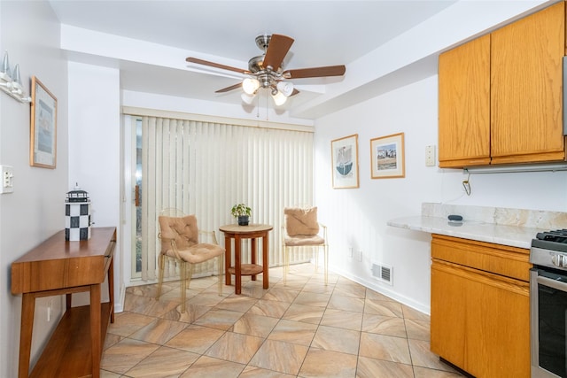 kitchen featuring stainless steel range with gas cooktop, light countertops, visible vents, a ceiling fan, and baseboards