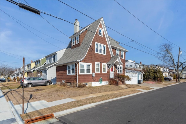 view of front of home featuring an attached garage, a residential view, a chimney, and roof with shingles