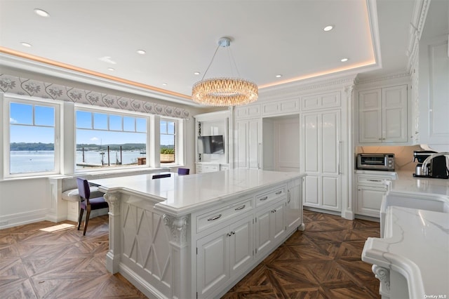 kitchen featuring light stone countertops, a kitchen island, white cabinets, and a raised ceiling