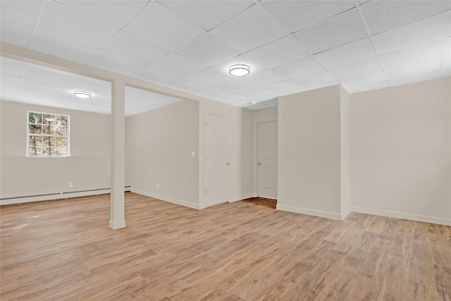 basement featuring light wood-style flooring, baseboards, baseboard heating, and a drop ceiling