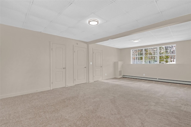 empty room featuring a baseboard heating unit, carpet, a paneled ceiling, and baseboards