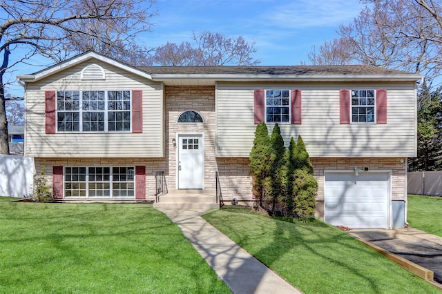 bi-level home with a front lawn, fence, aphalt driveway, stone siding, and an attached garage