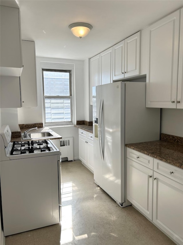 kitchen with radiator, white cabinets, a sink, dark stone counters, and white appliances