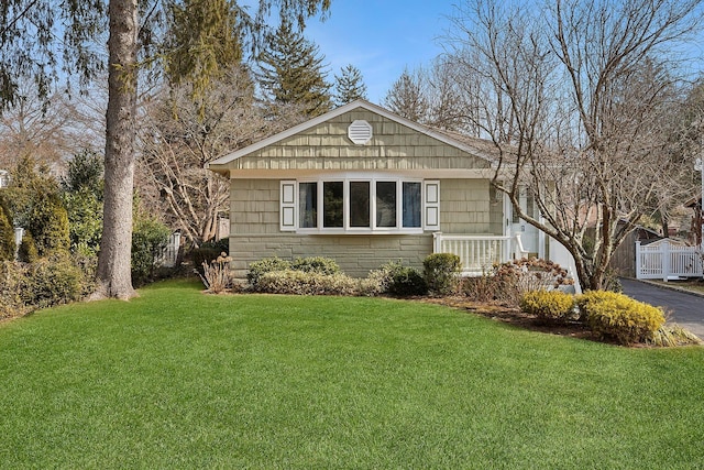 view of front of house with driveway, stone siding, fence, and a front lawn