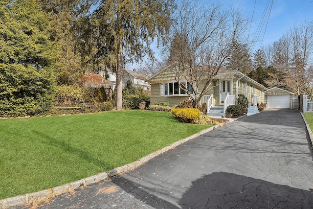 view of front of property with aphalt driveway, an outbuilding, a detached garage, and a front lawn