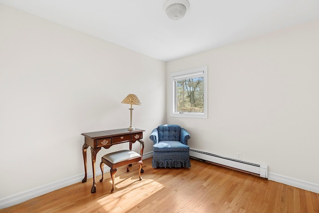 sitting room featuring a baseboard heating unit, light wood-style flooring, and baseboards