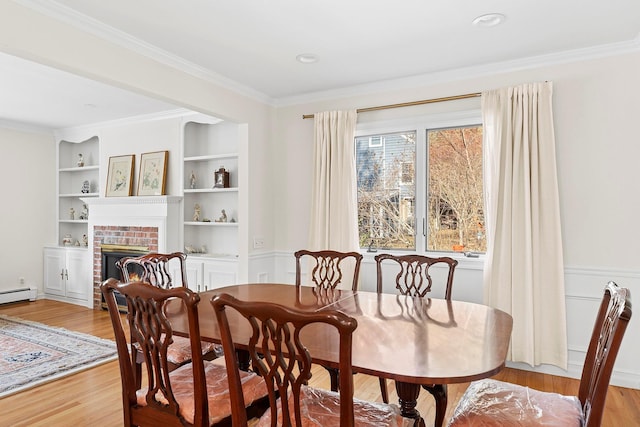 dining area featuring light wood-type flooring, a brick fireplace, built in shelves, and ornamental molding