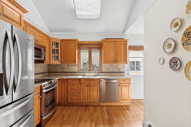 kitchen featuring light wood-style flooring, glass insert cabinets, appliances with stainless steel finishes, light stone counters, and a sink