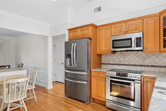 kitchen featuring light stone counters, brown cabinets, stainless steel appliances, visible vents, and glass insert cabinets