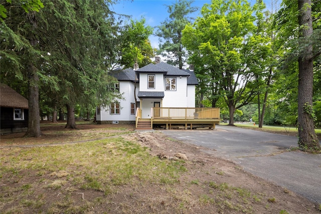 view of front of home with driveway, a shingled roof, and a wooden deck