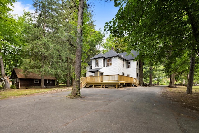 view of front of house with a shingled roof, a chimney, aphalt driveway, and a wooden deck