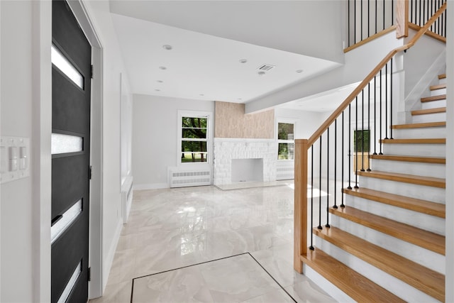 foyer entrance featuring visible vents, baseboards, marble finish floor, a brick fireplace, and radiator heating unit