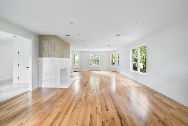 unfurnished living room featuring a fireplace, visible vents, baseboards, light wood-type flooring, and radiator heating unit